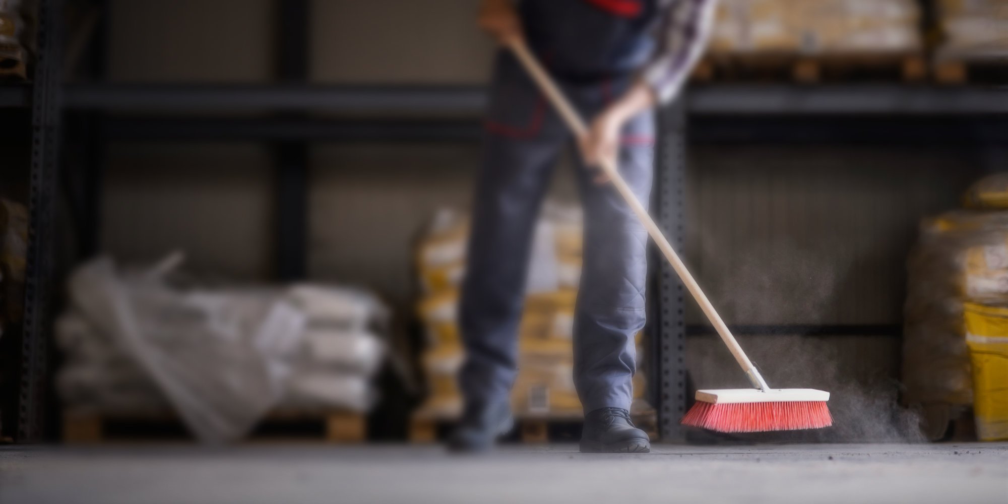 Anschnitt von Körper einer Person beim Fegen einer Werkstatt.