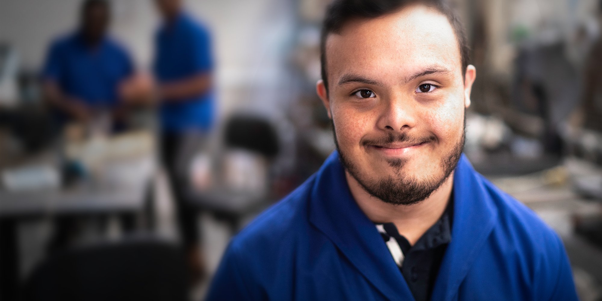 Junger Mann mit Behinderung in einer Werkstatt lächelt in die Kamera