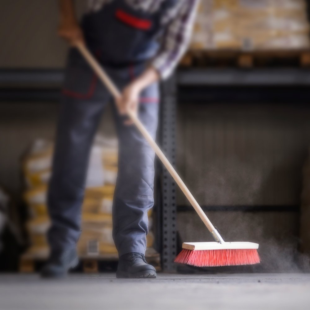 Anschnitt von Körper einer Person beim Fegen einer Werkstatt.