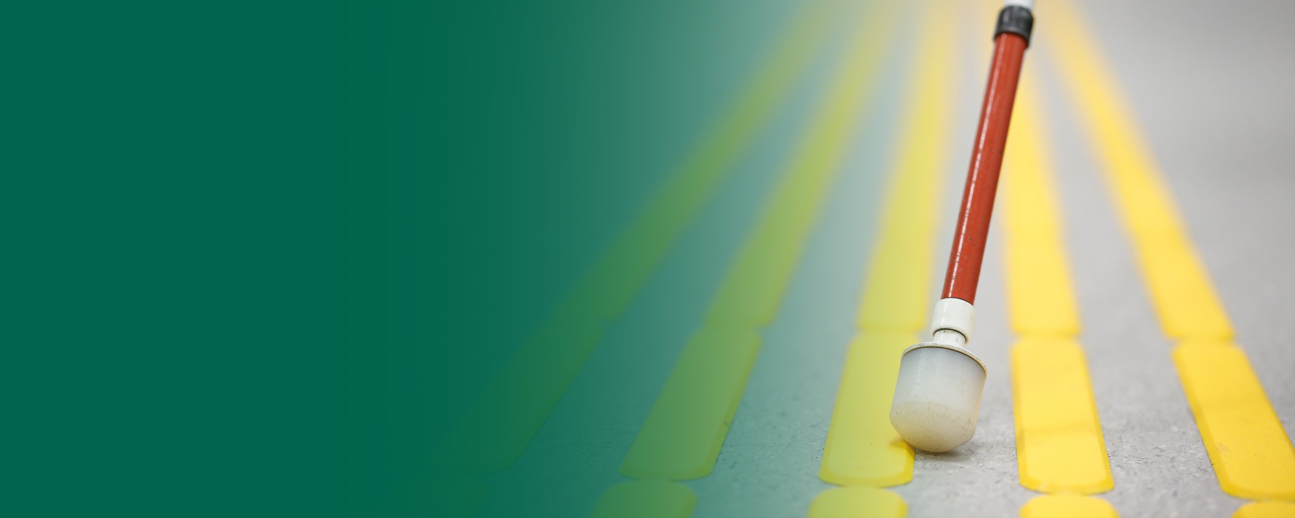 Nahaufnahme eines Langstocks auf einem Blindenleitsystem mit Verlaufsüberlagerung