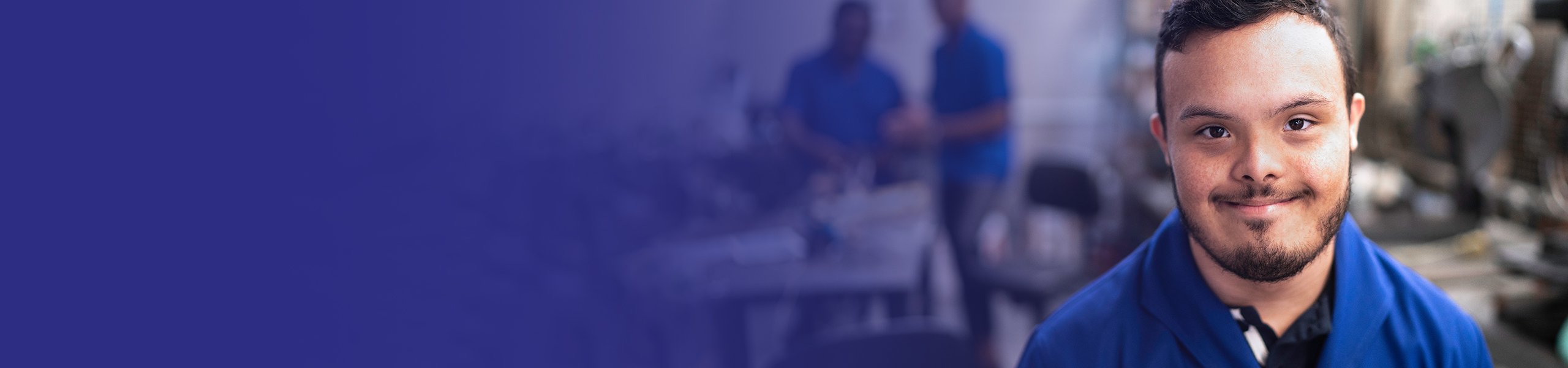 Junger Mann mit Behinderung in einer Werkstatt lächelt in die Kamera